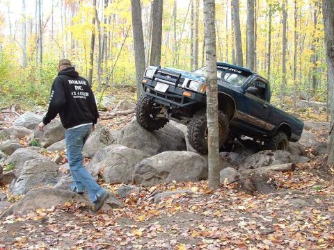 1977 Ford F-150 - Pickup truck attempting to traverse a difficult rocky terrain in a wooded area.