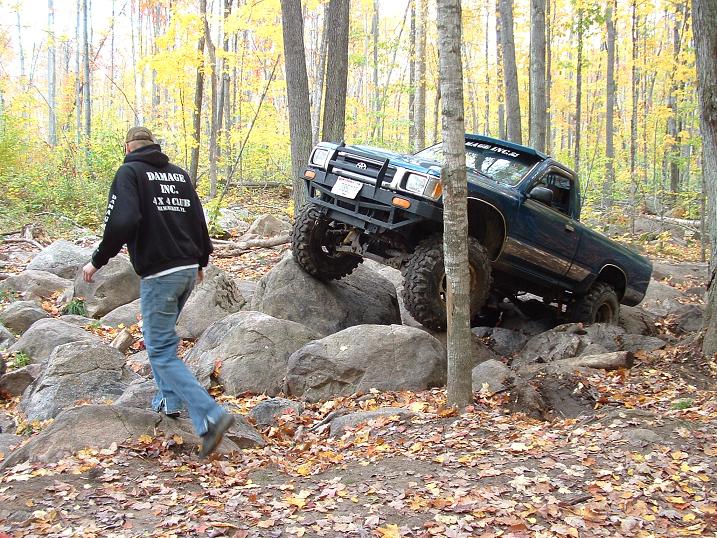 Off-road pickup truck with large tires navigating a rocky trail in a forest