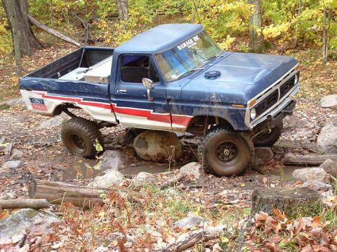 1977 Ford F-150 - This modified pickup truck is shown tackling a challenging off-road course with large rocks and mud.