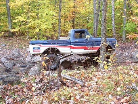 1977 Ford F-150 - A lifted Ford F-Series truck navigates a rocky trail in a wooded area during autumn.