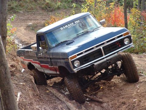 1977 Ford F-150 - This lifted pickup truck navigates a challenging off-road course with steep inclines and muddy terrain.