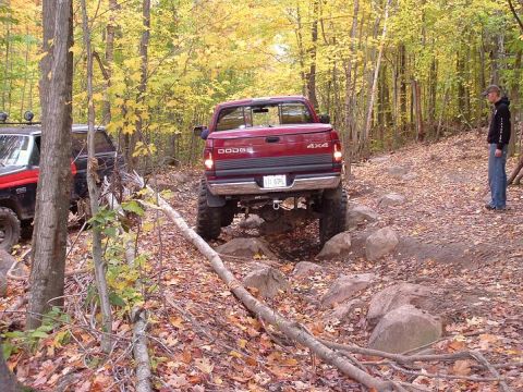 1977 Ford F-150 - Two off-road vehicles tackle a challenging rocky path in a wooded area during autumn.