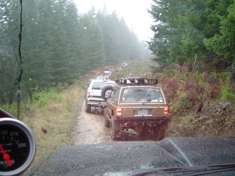 1989 Ford Bronco - Multiple off-road vehicles navigate a muddy path through a dense forest during an event.