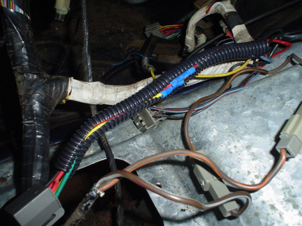 Close-up of a vehicle's wiring harness with black protective conduit and various colored wires
