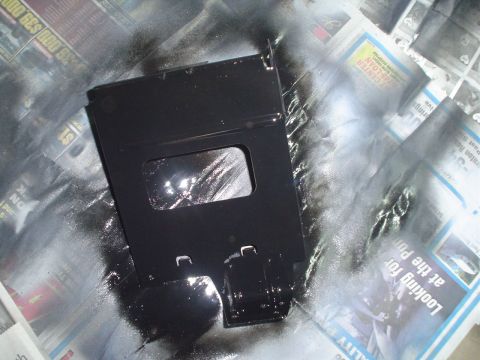 1984 Ford Bronco - A metal part is being spray painted black, resting on a surface covered with newspapers.