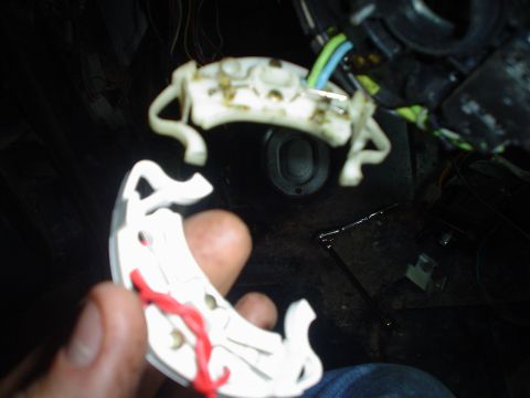 1984 Ford Bronco - A hand holds a detached white plastic wiring harness connector with red wires against a dark background of car interior components.