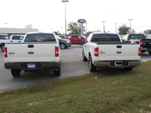2004 Ford F-150 - Two white 2004 Ford F-150 trucks are parked in a lot, with a Ford dealership sign visible in the background.