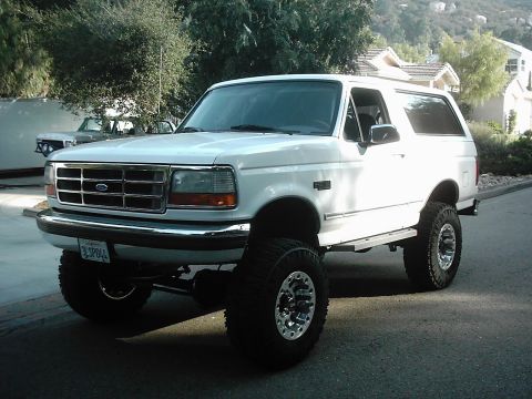 1978 Ford Bronco - A white SUV with large tires and chrome wheels is parked on a street, with another vehicle visible in the background.