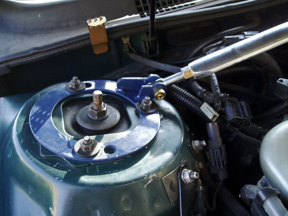 Blue adjustable camber plate on strut tower with polished aluminum strut brace in green engine bay
