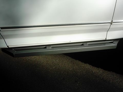 1978 Ford Bronco - Side view of a white SUV's lower body panel and step bars.