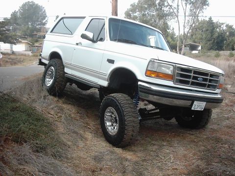 1978 Ford Bronco - This lifted white Ford Bronco SUV is shown from a three-quarter front angle on a grassy hill.