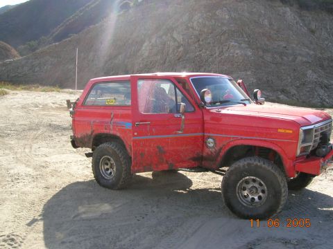 1985 Ford Bronco - Red SUV parked on dirt with mountains in the background. Date stamp visible.