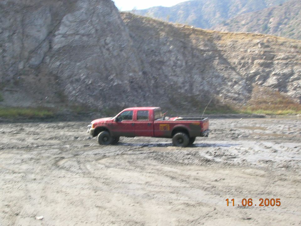 Red pickup truck with a crew cab and long bed parked in a muddy, rocky area. A date stamp reads 11.06.2005