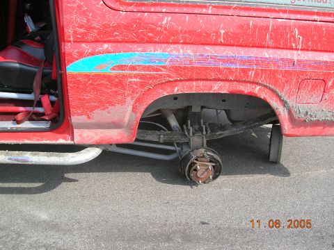 1985 Ford Bronco - A red van with a missing rear wheel and visible racing seats is parked on asphalt.