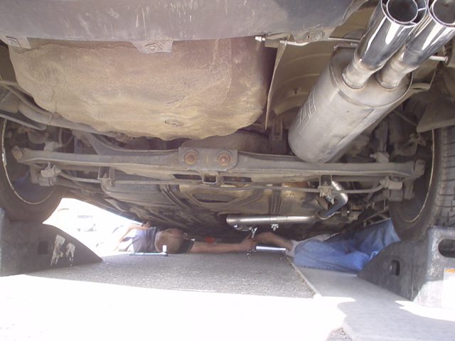 Underside of a car showing the exhaust system and a person working on it