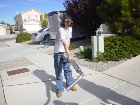 1993 Ford Probe - A person holds a new exhaust pipe in a suburban driveway next to a trailer and a car.