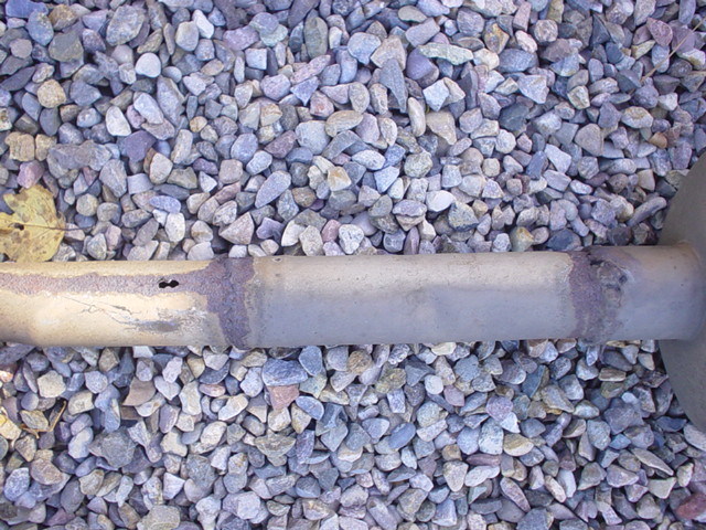 Exhaust pipe with rust and two small holes, lying on gravel