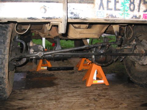 1991 Ford Explorer - Low front-underside view of a lifted 4x4 SUV supported on three orange jack stands over plywood, showing the solid front axle, differential…
