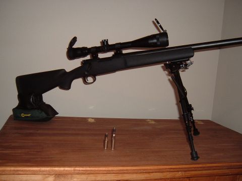 1979 Ford Bronco - A rifle with a scope and bipod rests on a wooden table next to two bullets.