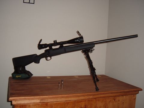 1979 Ford Bronco - A rifle equipped with a scope and bipod rests on a wooden surface, with two bullets in the foreground.