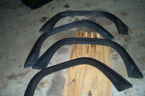1978 Dodge Power Ram - Set of four black fender flares laid out on a wooden board on a concrete floor.