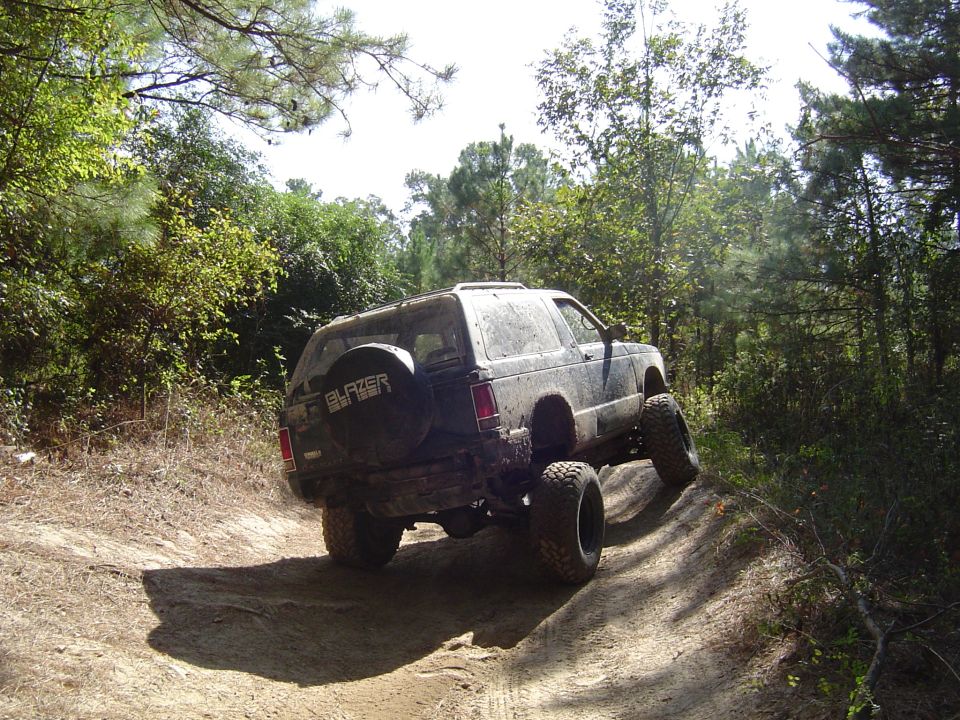 Lifted black Chevy S-10 Blazer with Blazer spare tire cover on a sandy wooded off-road trail