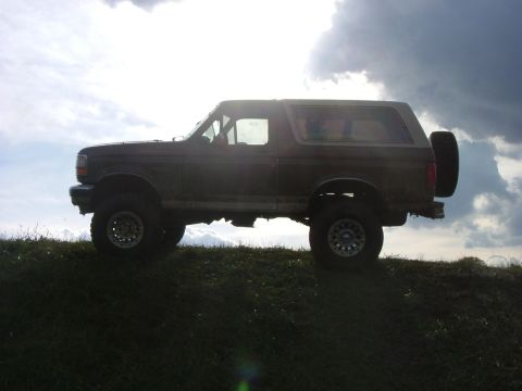 1993 Ford Bronco - A Ford Bronco is parked on a grassy incline against a dramatic, cloudy sky.