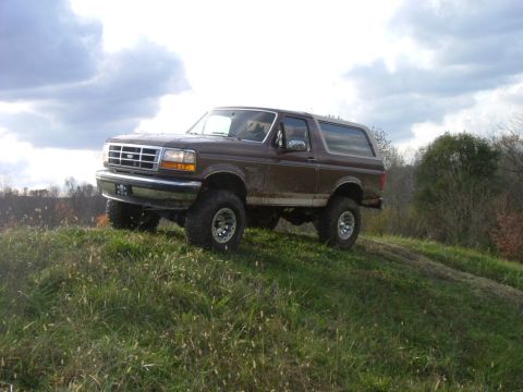 1993 Ford Bronco - A brown Ford Bronco is parked on a grassy incline under a cloudy sky.
