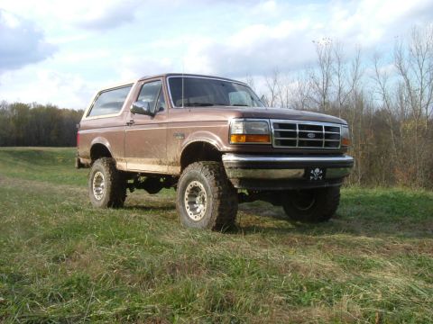 1993 Ford Bronco - Brown 1993 Ford Bronco with lifted suspension and off-road tires sits in a field.