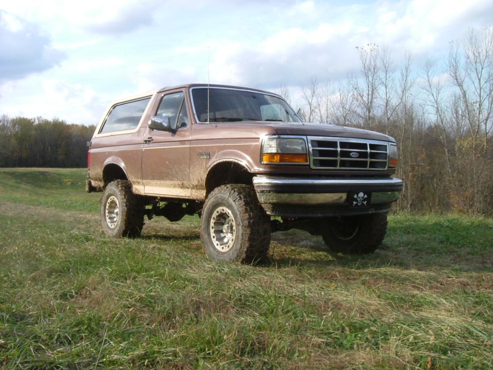 Lifted brown two-door Bronco on mud tires parked in a grassy autumn field