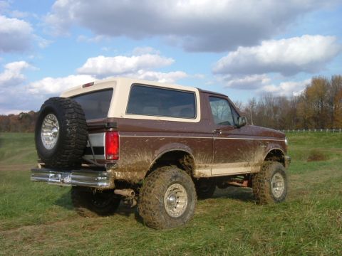 1993 Ford Bronco - A muddy Ford Bronco sits in a field under a cloudy sky.
