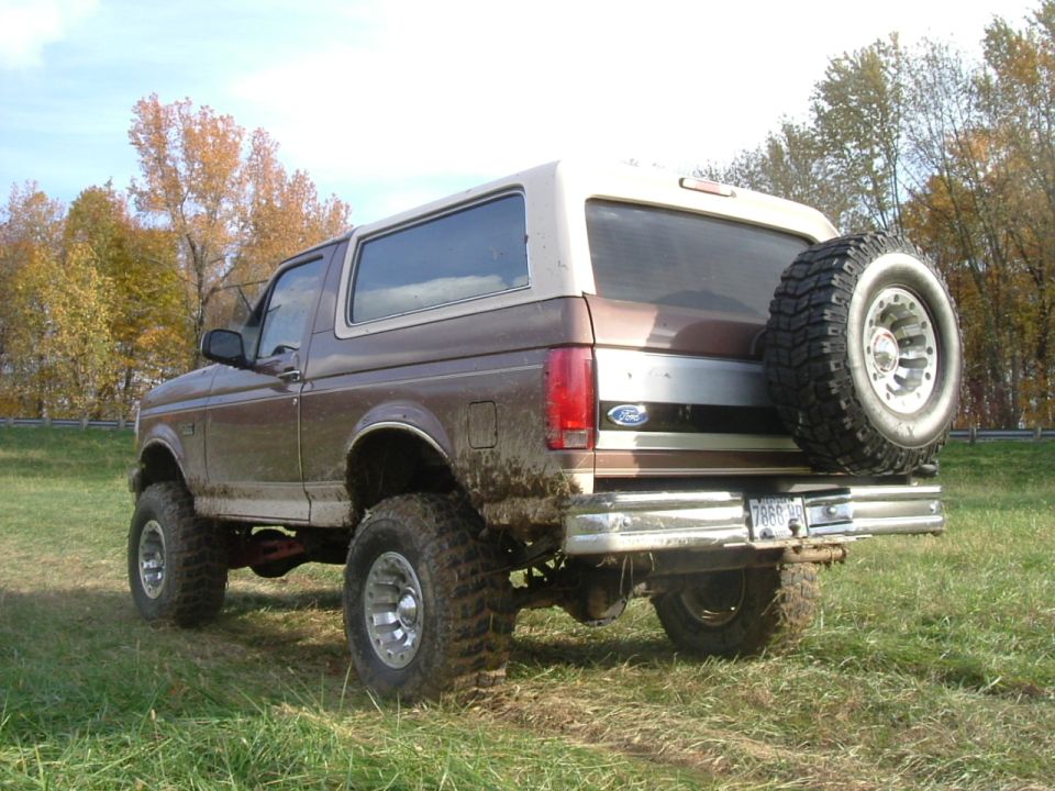 Lifted brown and tan Ford Bronco with rear-mounted spare and muddy mud-terrain tires in a field