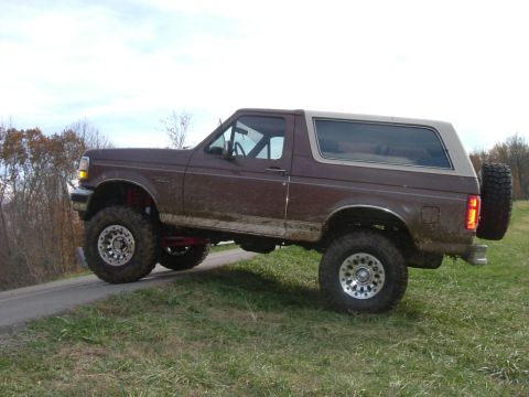 1993 Ford Bronco - Brown 1993 Ford Bronco with lifted suspension and off-road tires parked on a grassy incline.