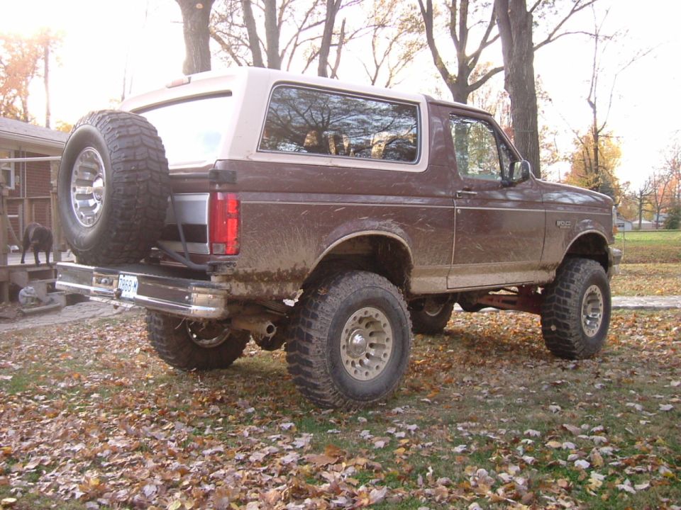 Muddy lifted brown and white Ford Bronco with rear spare carrier, rear 3/4 view