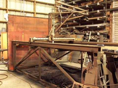1979 Ford Bronco - A large industrial welding machine is set up in a workshop, surrounded by metal stock and equipment.