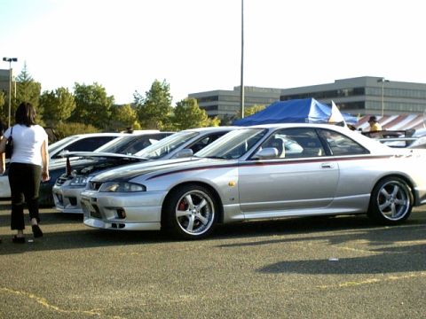 1995 Ford Bronco - Several cars are parked in a lot, including a silver coupe with racing stripes.