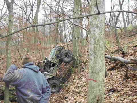 1992 Ford Bronco - An off-road vehicle is stuck on a steep, wooded slope, with a person observing the situation.
