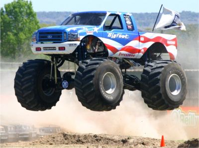 1991 Ford Bronco - A Bigfoot monster truck soars through the air, decorated with a patriotic red, white, and blue paint scheme.