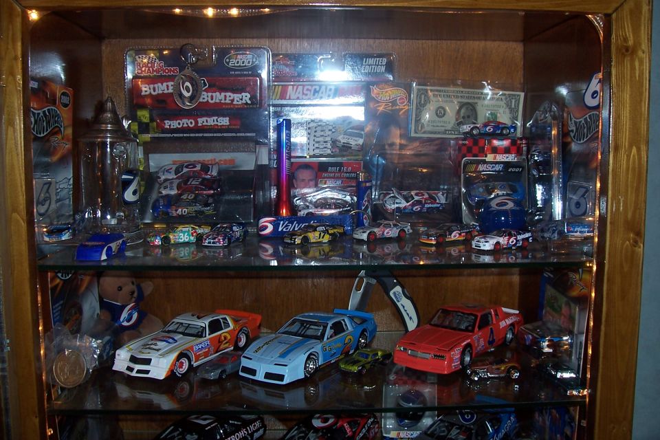 Display case filled with model cars, NASCAR memorabilia, and some currency