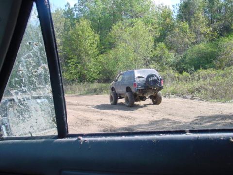 1992 Chevrolet S10 - An SUV drives on a dirt road surrounded by trees, with a spare tire mounted on the rear.