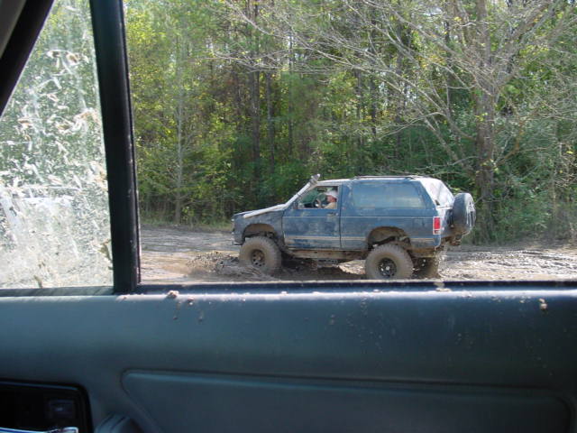 Dark blue SUV driving through mud, spare tire on rear door, aftermarket wheels