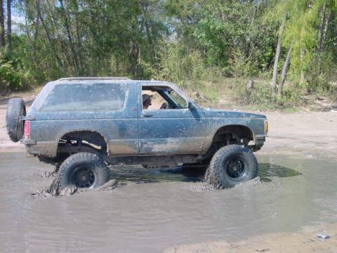 1992 Chevrolet S10 - A blue SUV navigates through a muddy terrain, with its tires deep in the water.
