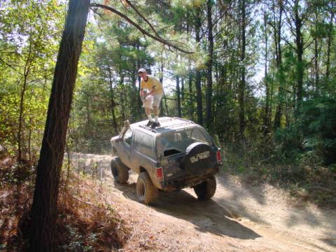 1992 Chevrolet S10 - A man stands atop a black Chevrolet K5 Blazer as it navigates a dirt trail through a wooded area.