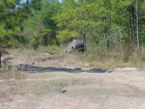 1992 Chevrolet S10 - An SUV is seen from the rear, driving through a challenging muddy terrain surrounded by dense forestation.