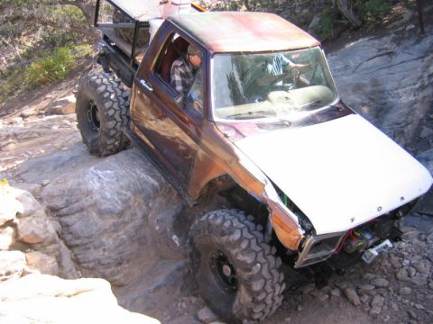 1981 Ford Bronco - Heavily modified pickup truck with oversized tires is shown off-roading on a rocky trail.