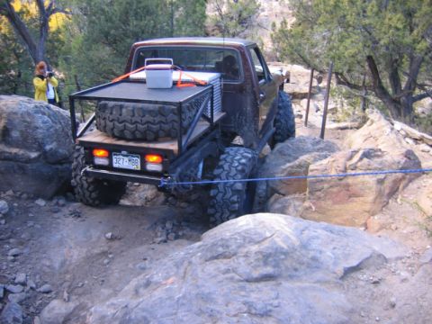 1981 Ford Bronco - A modified pickup truck is shown off-roading on a rocky trail, with a person observing in the background.