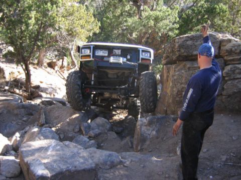 1981 Ford Bronco - A heavily modified off-road vehicle tackles a challenging rocky trail with a person guiding.