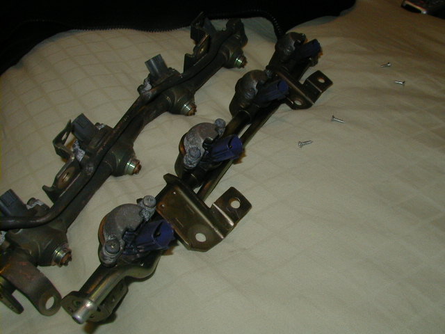 Two fuel injector rails with blue connectors on a textured surface