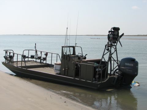 1989 Ford Bronco - A utilitarian boat with a raised engine mount and outboard motor sits partially on the sand near the water.