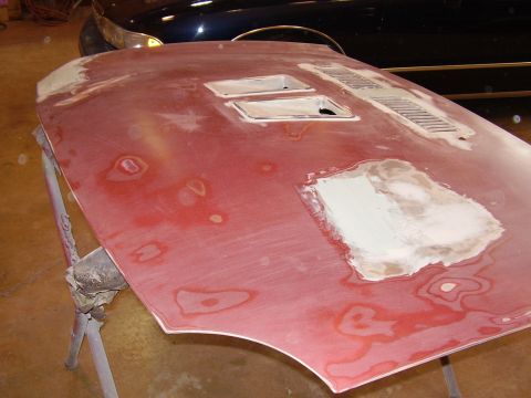 1997 Ford Taurus - A car hood is shown with body filler and primer, ready for paint work. A dark colored vehicle is visible behind it.